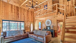 A wooden cabin interior with a large leather sofa, a chandelier, and a wooden staircase. - Furnished Patio & Fire Pit: Pinetop Cabin! (Pinetop)