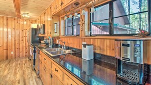 A wooden cabin kitchen with a large island, stainless steel appliances, and a view of the forest. - Furnished Patio & Fire Pit: Pinetop Cabin! (Pinetop)