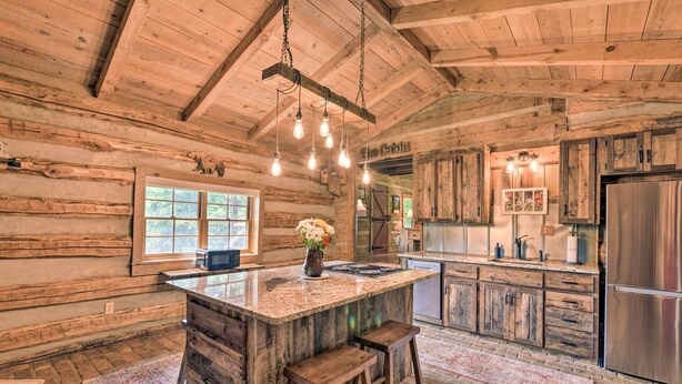 Une cuisine de style rustique, aménagée comme un chalet, avec des murs en bois, un grand îlot central doté de tabourets et un réfrigérateur en acier inoxydable.