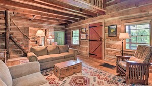 L’intérieur d’un chalet rustique en rondins de bois, avec un canapé, un fauteuil et une commode en bois.