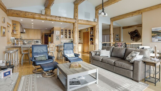 A spacious living area with a wooden ceiling, a sofa, a coffee table, and a dining area with bar stools. - Stunning Sheridan Ranch Villa: Mountain View! (Sheridan)