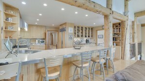 A modern kitchen with wooden beams, a central island with bar stools, and built-in cabinetry. - Stunning Sheridan Ranch Villa: Mountain View! (Sheridan)