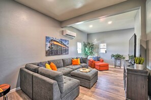 A modern living room with a sectional sofa, a small orange ottoman, and a flat-screen TV on a wooden cabinet. - Family-friendly Williams Cabin w/ Gas Grill (Williams)
