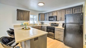 A modern kitchen with dark wooden cabinets, stainless steel appliances, and a central island with a sink and stools. - Cozy Blackfoot Apartment: Pets Welcome! (Blackfoot)