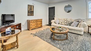 A living room with a television, wooden dresser, sofa with patterned cushions, and a round coffee table. - Cozy Blackfoot Apartment: Pets Welcome! (Blackfoot)