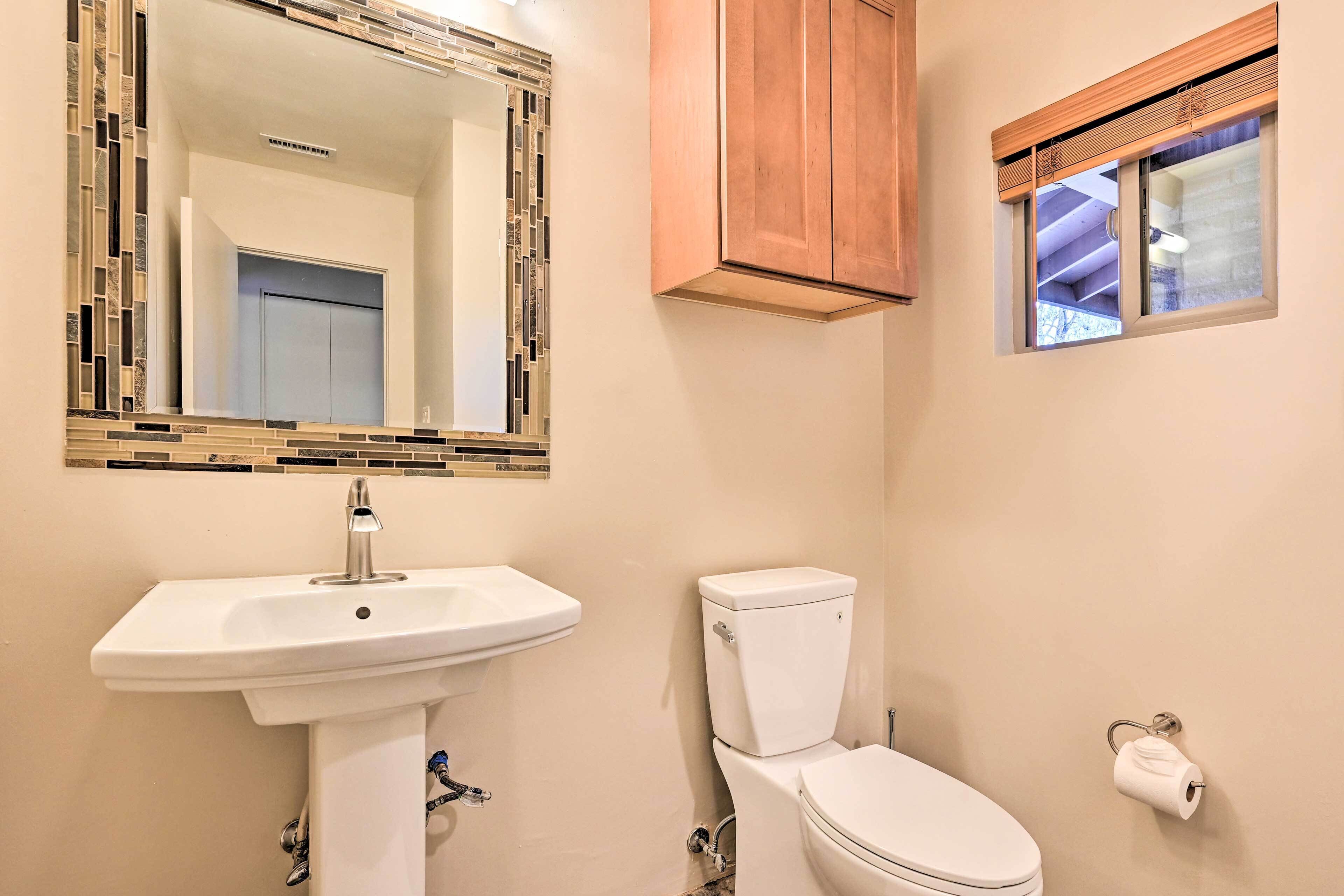 A bathroom with a white sink, a toilet, a mirror with a mosaic frame, and a window with a wooden blind.