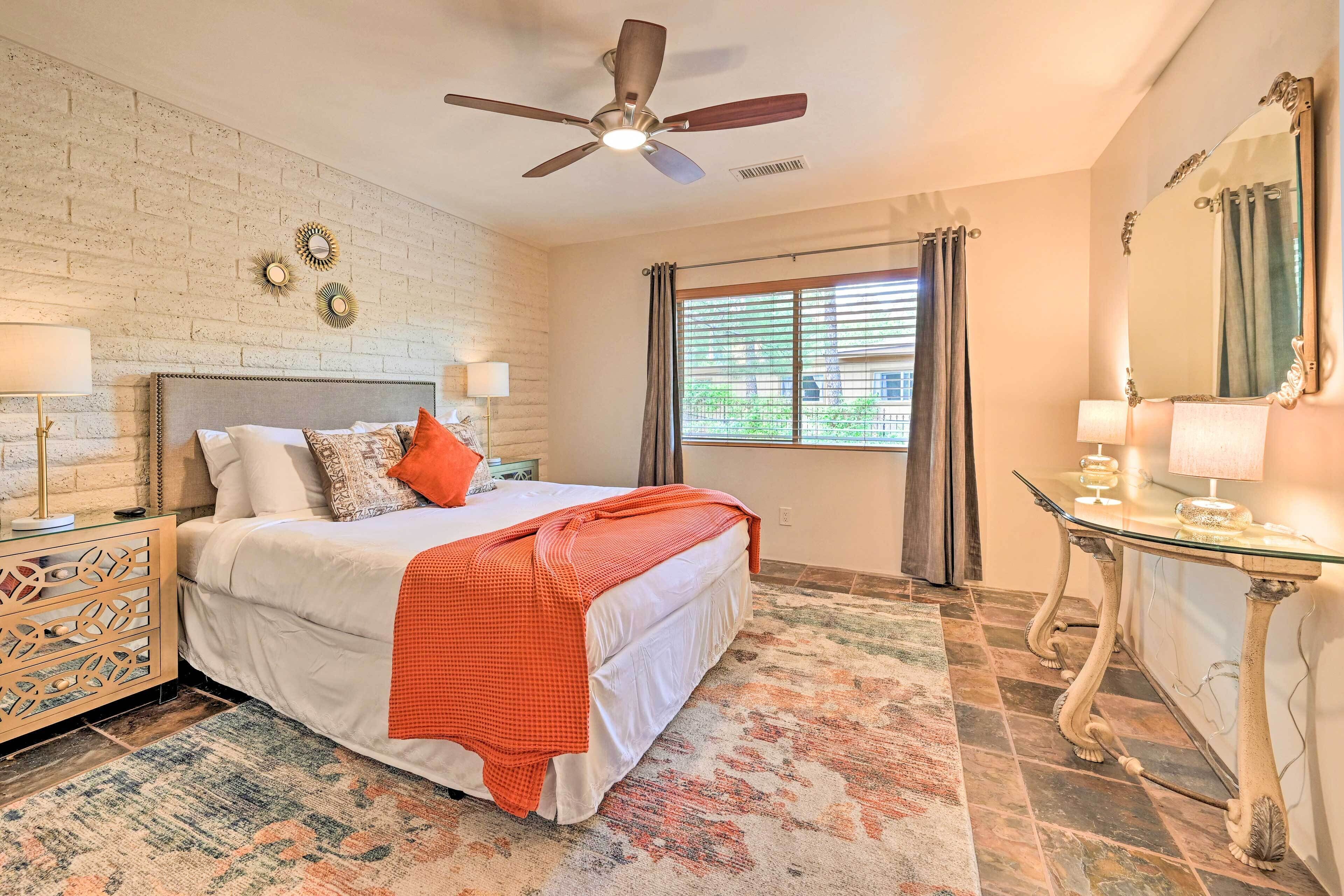 A bedroom with a bed, a ceiling fan, a window with curtains, a bedside table, and a mirror.