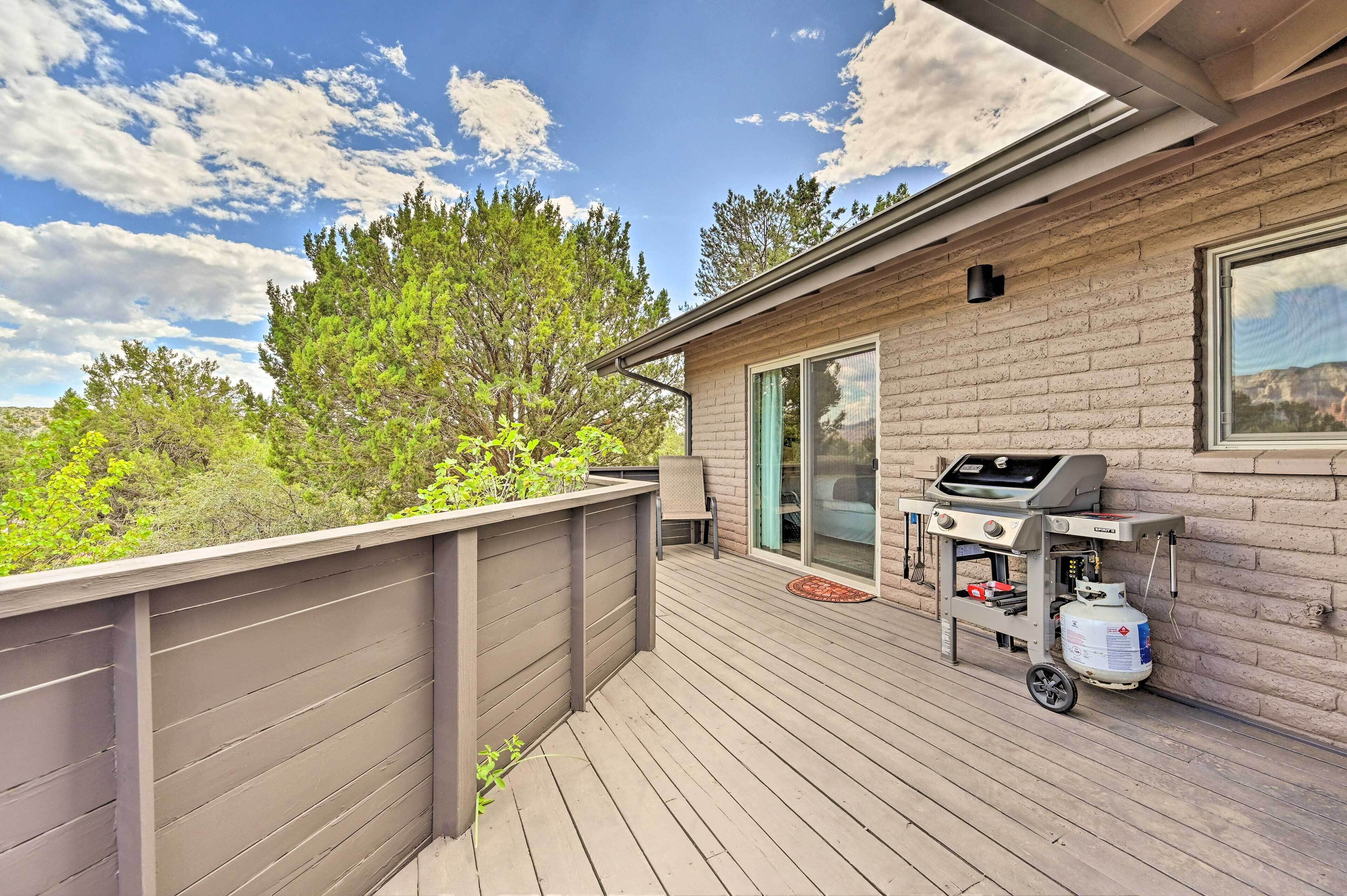 A deck with a grill and propane tank, a sliding glass door, and a view of trees and sky.