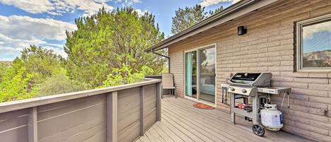 A deck with a grill and propane tank, a sliding glass door, and a view of trees and sky.