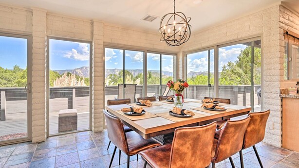 A spacious dining area with a large table set for six, surrounded by leather chairs, large windows offering a mountain view, and a modern chandelier. - Patio & Panoramic Desert Views: Sedona Getaway! (Sedona)