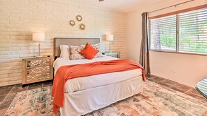 A bedroom with a bed, two bedside tables, a ceiling fan, a window with blinds, and a brick wall. - Patio & Panoramic Desert Views: Sedona Getaway! (Sedona)