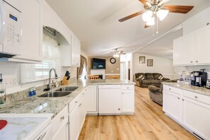 A spacious kitchen with white cabinets, granite countertops, and a dishwasher. There is a ceiling fan, a television, and a dining area with a table and chairs. - Cozy New Bern Getaway < 2 Mi to Trent River! (New Bern)