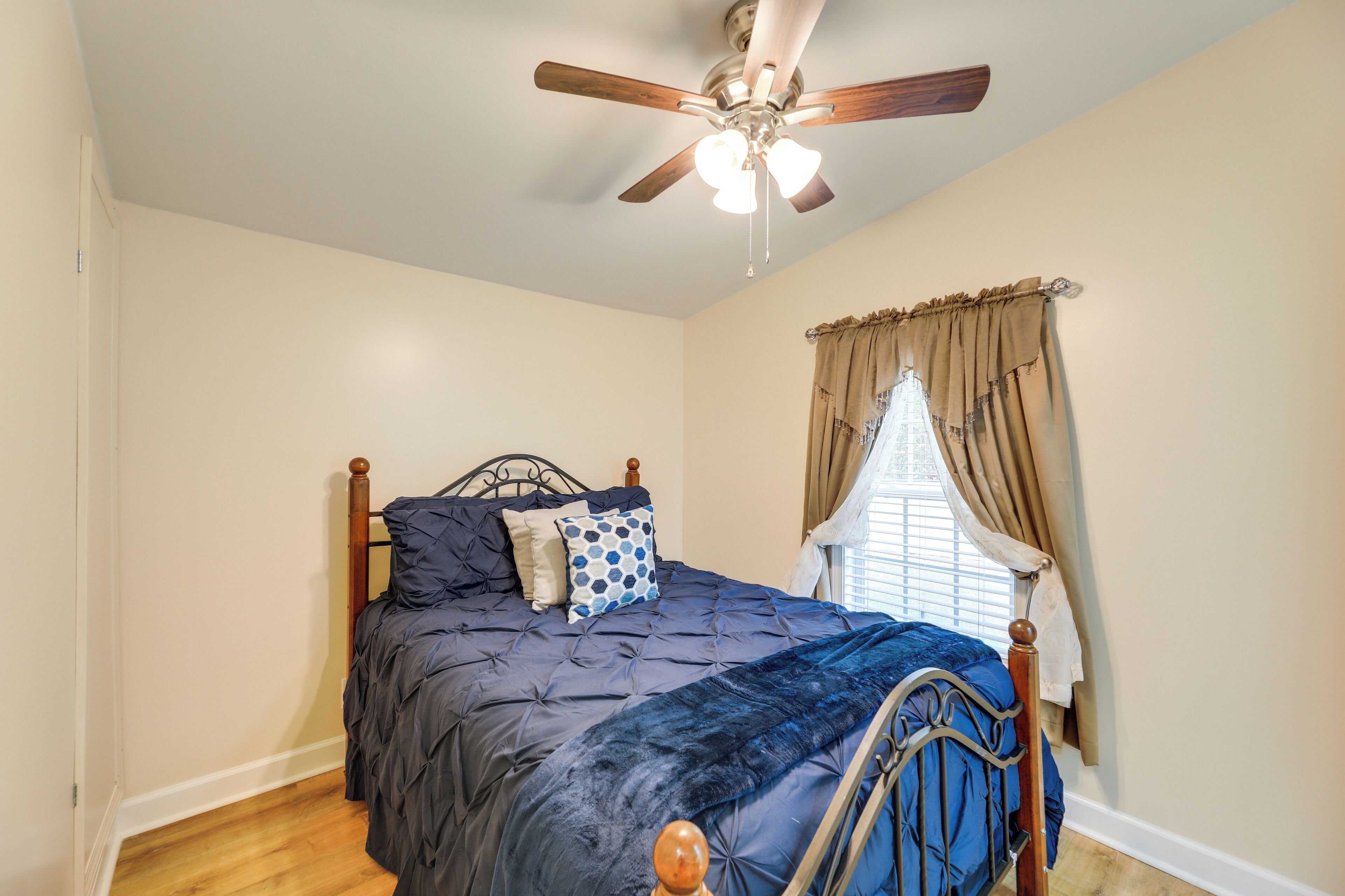A bedroom with a bed, a ceiling fan, a window with curtains, and a wooden floor.