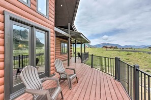 Uma cabana de madeira com varanda, duas cadeiras Adirondack e vista para as montanhas.