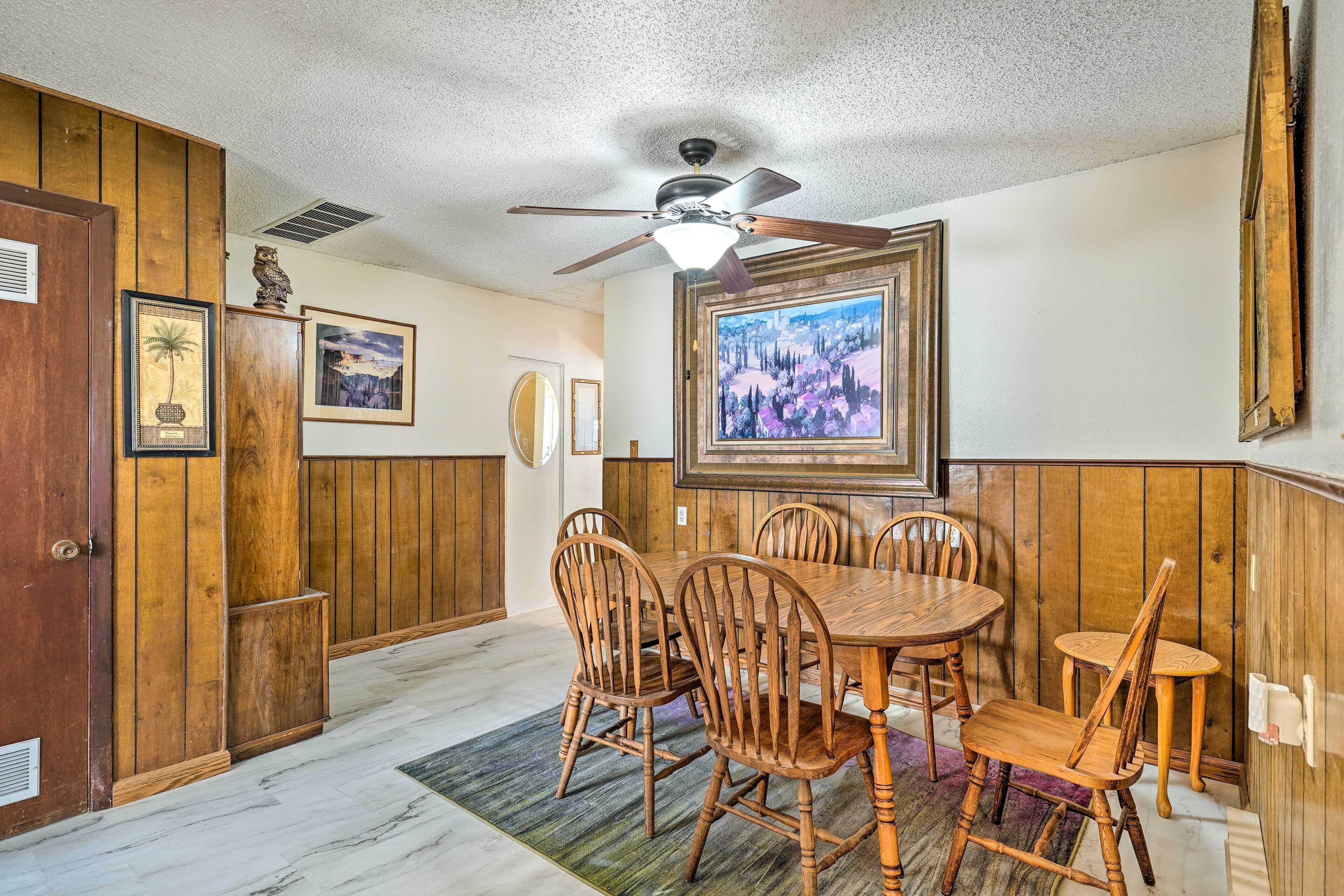 A dining area with wooden paneling, a ceiling fan, and framed artwork on the walls.