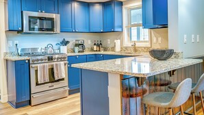 Une cuisine moderne avec des meubles bleus, des appareils en acier inoxydable, des comptoirs en granit et un îlot central doté de tabourets de bar.