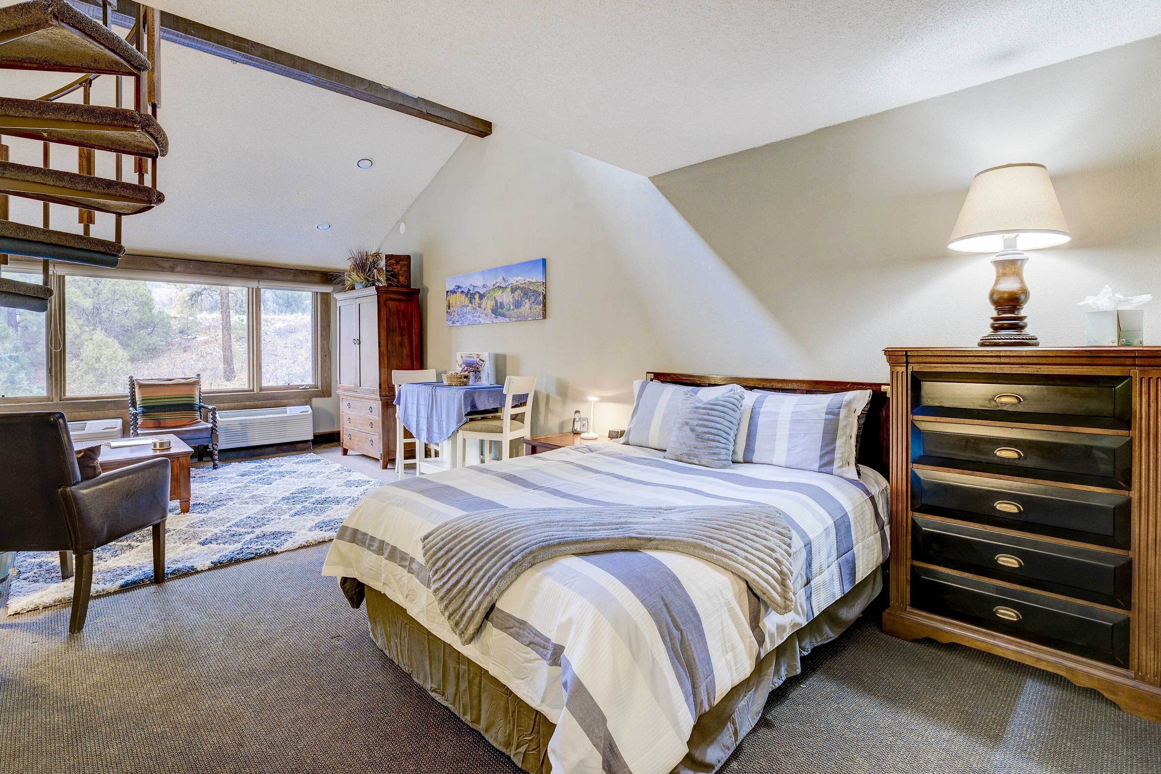 A bedroom with a bed, a dresser, a lamp, a chair, a desk, and a painting on the wall.