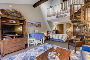 Un loft spacieux doté d’un grand téléviseur, d’un coin repas, d’une chambre et d’un escalier en colimaçon.