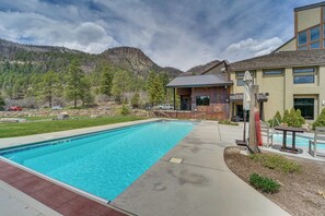 Une piscine avec vue sur les montagnes, un bâtiment au design moderne et une pelouse bien entretenue.