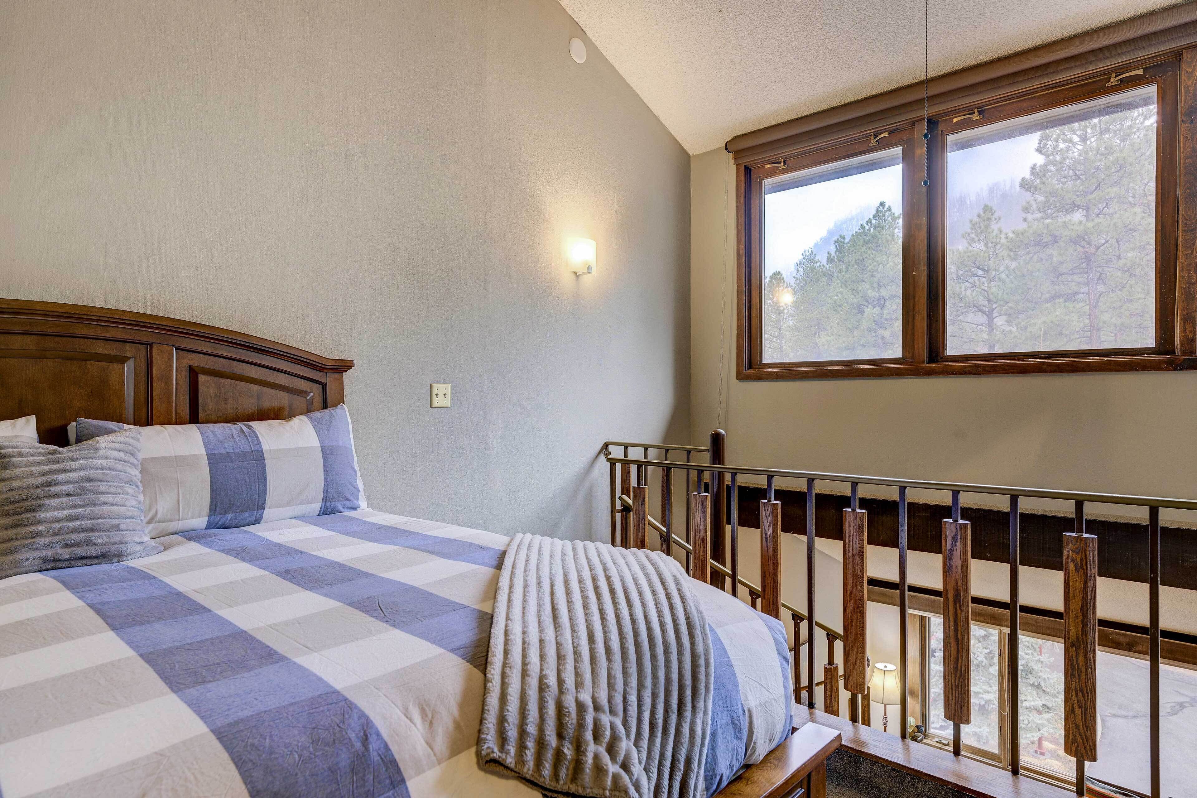 Ein Schlafzimmer mit einem großen Bett, einem Fenster mit Blick auf Bäume und einem Holzlaufgeländer.