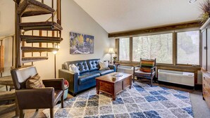 A living room with a blue sofa, a wooden coffee table, a fireplace, and a spiral staircase. - Durango Lofted Studio ~ 9 Mi to Purgatory Resort! (Durango)