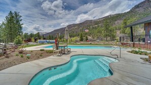 A swimming pool with a wooden deck, surrounded by a landscaped area with trees and a mountain backdrop. - Durango Lofted Studio ~ 9 Mi to Purgatory Resort! (Durango)