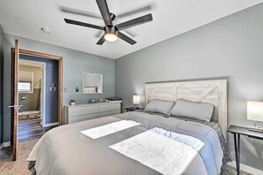 A bedroom with a bed, bedside tables, a ceiling fan, and a door leading to another room. - Charming Wausau Cottage: On-site Lake Access! (Wausau)