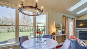 Un coin repas avec une table ronde, des chaises et un lustre. On y trouve également une cheminée et un grand miroir au mur.