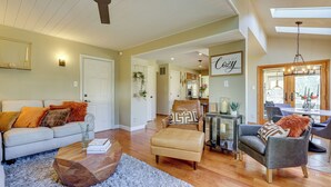 Un salon spacieux comprenant un canapé, un pouf et des fauteuils, un plancher en bois et un ventilateur de plafond.