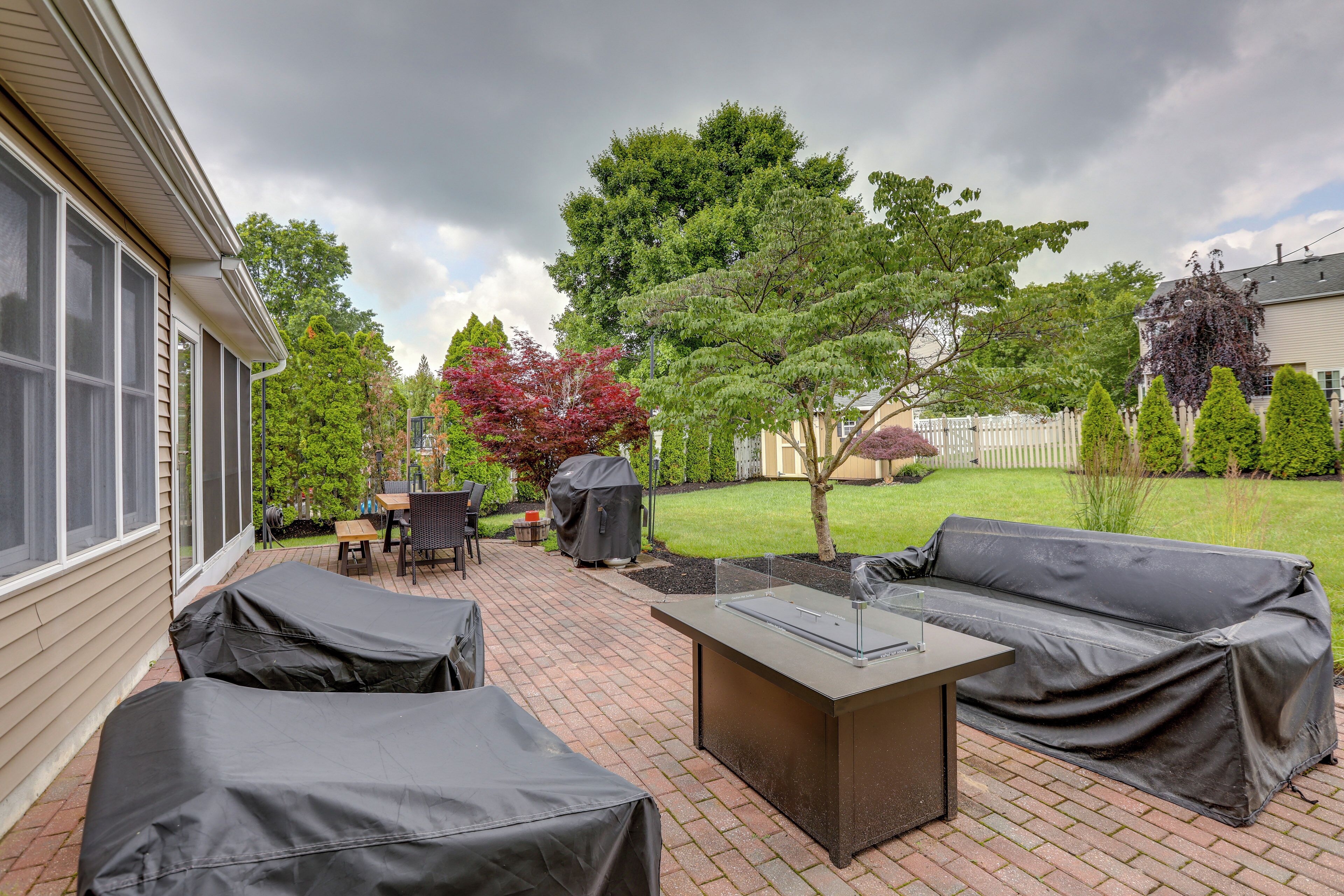 A patio with covered furniture, a grill, and a small tree.