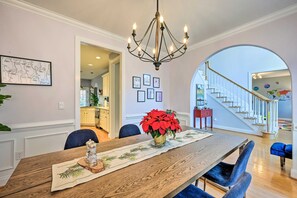 A dining area with a wooden table, blue chairs, a chandelier, and a staircase leading to another room. - Tranquil Greensboro Home w/ Fire Pit! (Greensboro)