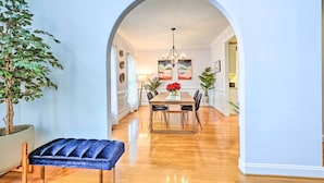A dining area with a wooden table, chairs, and a chandelier. There is a potted plant and a bench in the foreground. - Tranquil Greensboro Home w/ Fire Pit! (Greensboro)