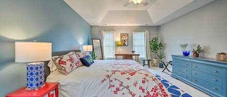 A bedroom with a bed, a red nightstand, a blue dresser, a ceiling fan, and a desk with a chair.