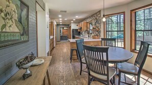 A kitchen with wooden cabinets, a dining table with chairs, and a large window with a view of trees. - Screened Porch, Fenced Yard: Lakeside Retreat! (Lakeside)