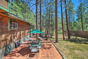 A wooden cabin with a patio area, outdoor seating, and a view of a forest. - Screened Porch, Fenced Yard: Lakeside Retreat! (Lakeside)