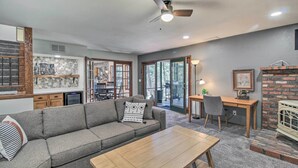 A modern living room with a sofa, coffee table, and a fireplace. There is a dining area with a table and chairs, and a kitchen with a stone backsplash. - Screened Porch, Fenced Yard: Lakeside Retreat! (Lakeside)