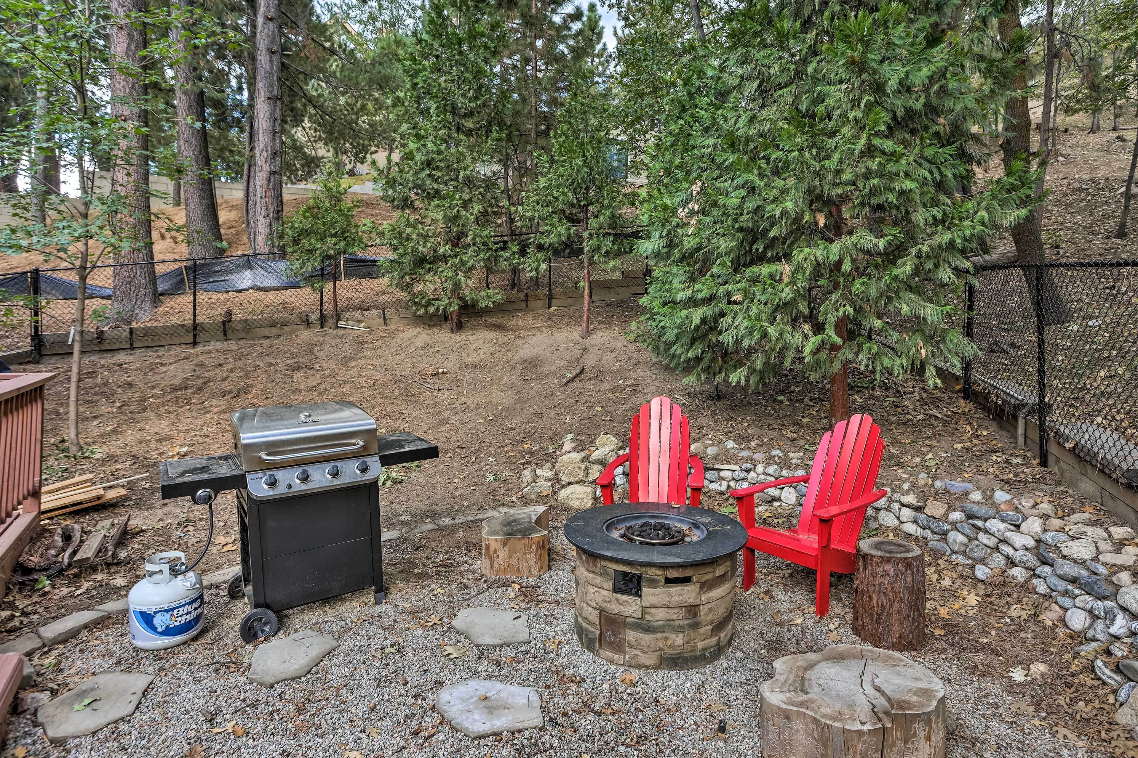An outdoor patio with a grill, a fire pit, and red Adirondack chairs.