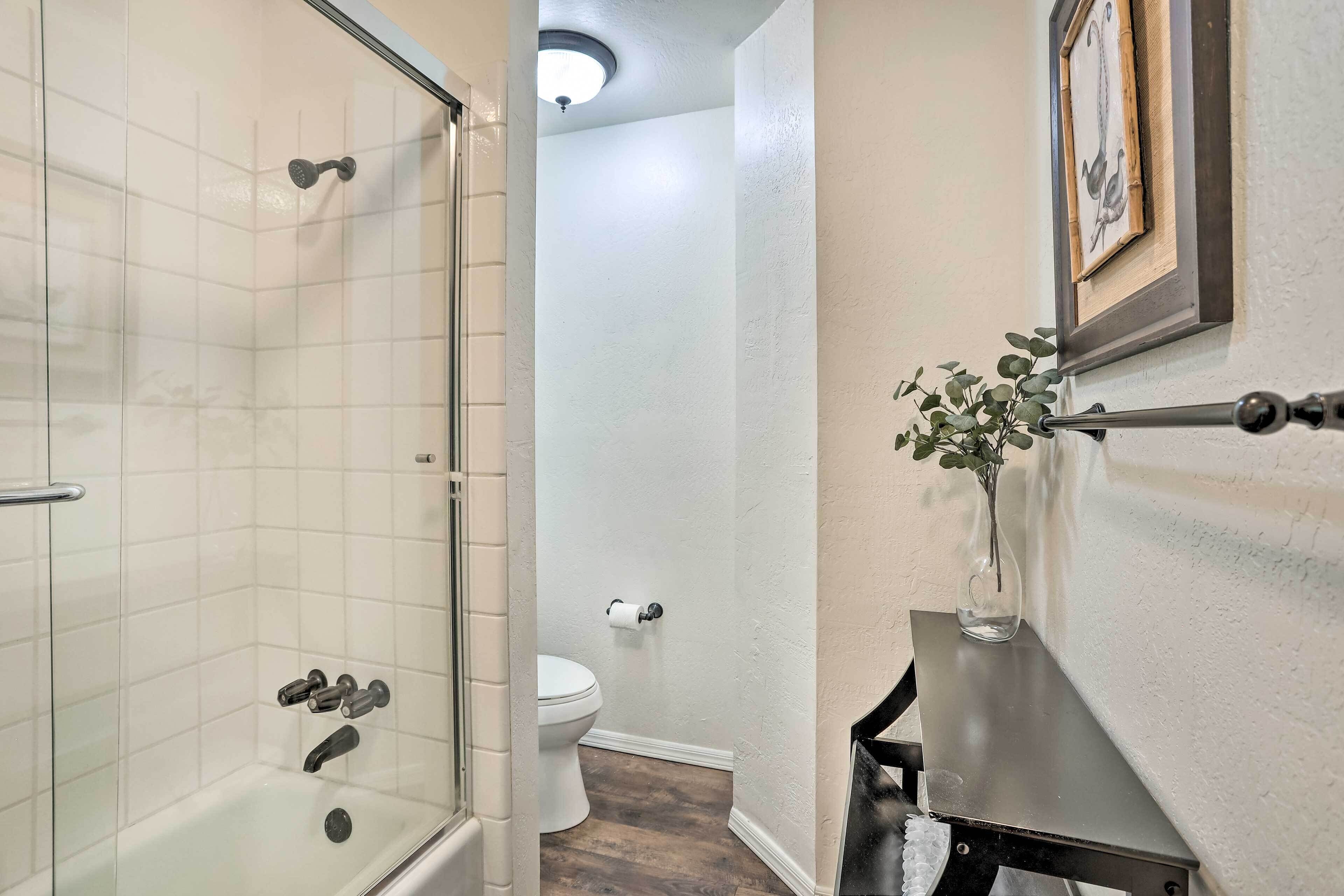 A bathroom with a glass-enclosed shower, a toilet, and a small vanity with a vase of flowers.