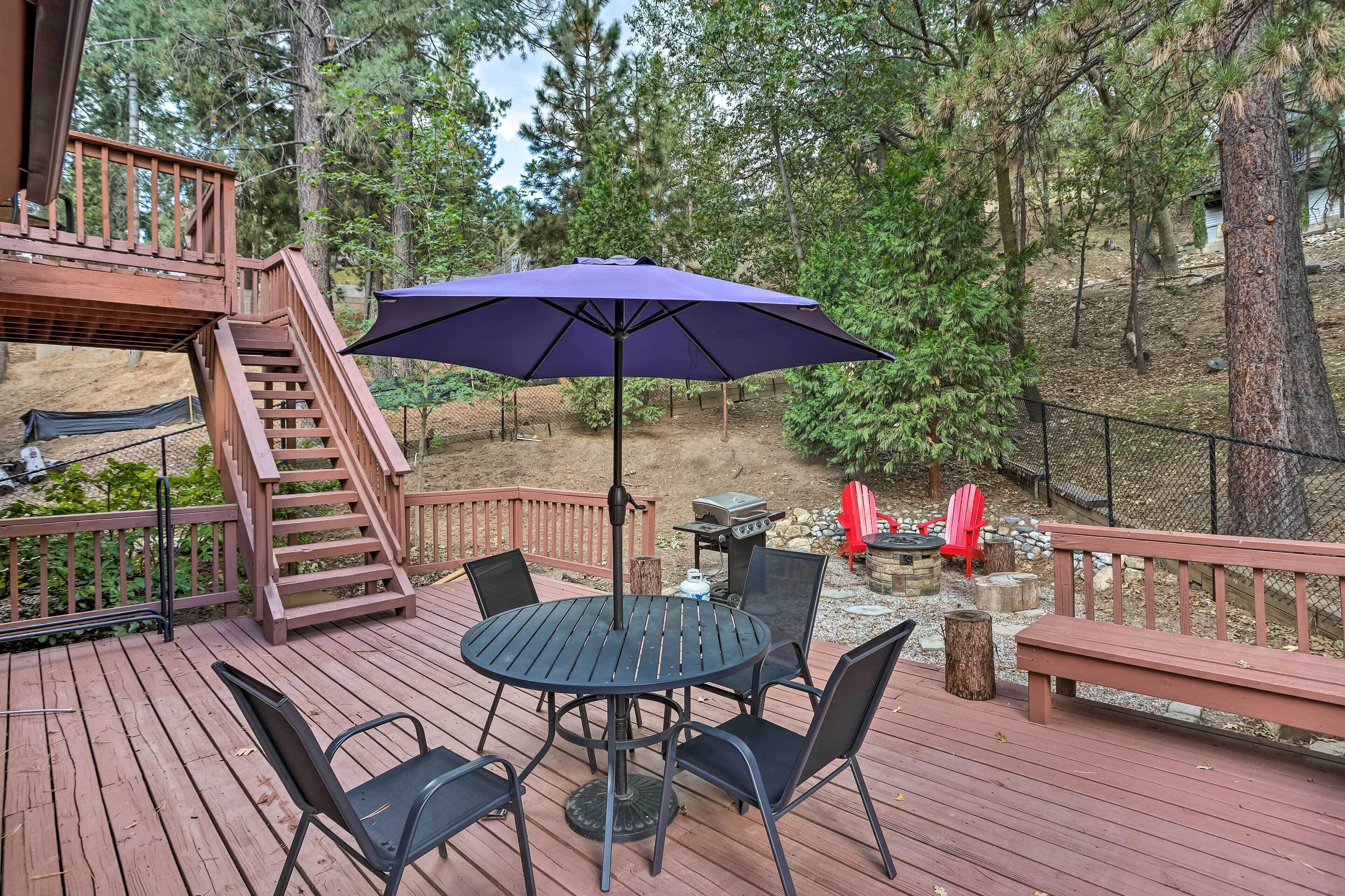 A wooden deck with a round table and chairs, a purple umbrella, and a red Adirondack chair.