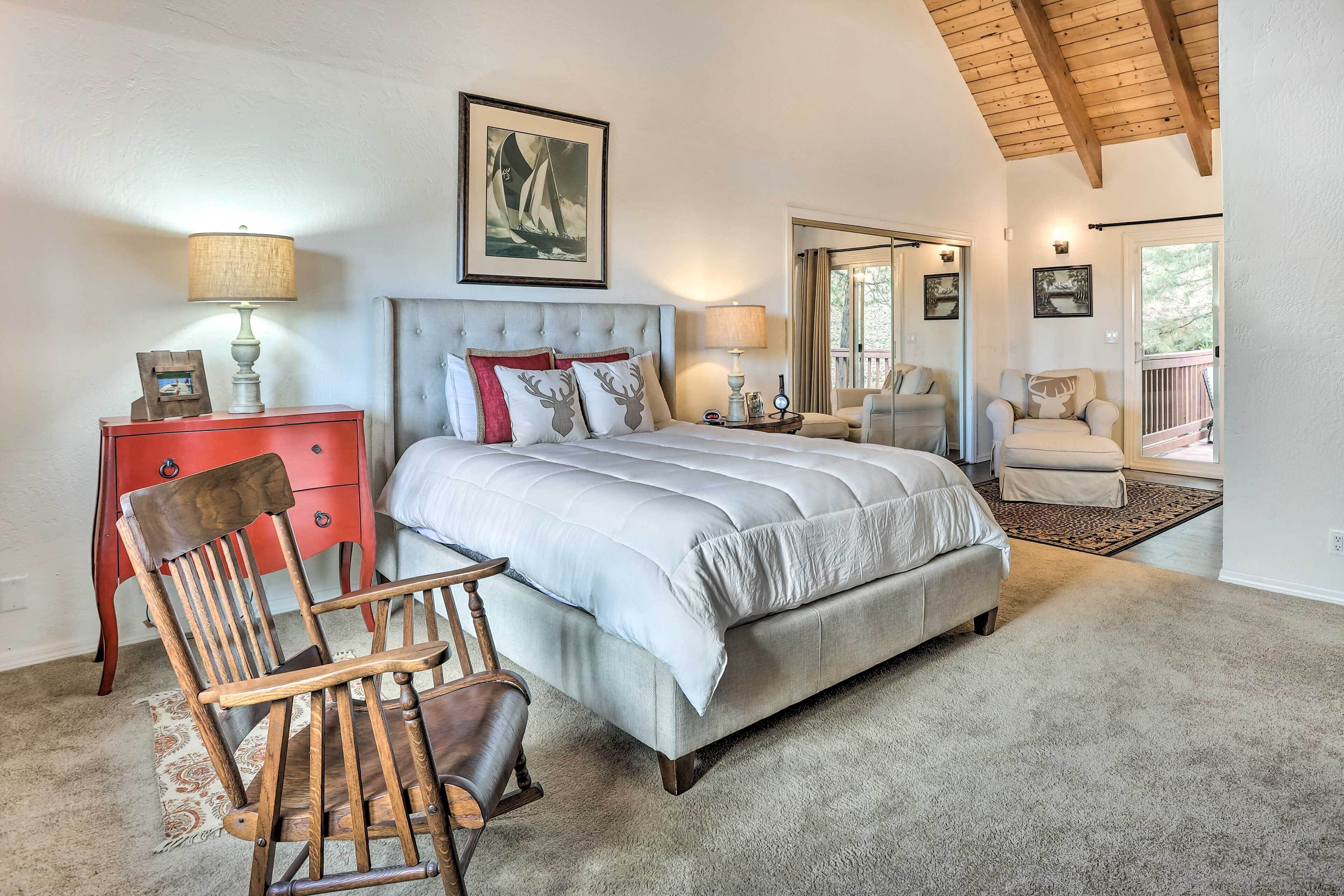 Un dormitorio con una cama grande, una silla de madera, un aparador rojo y una puerta que da a un balcón.