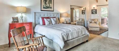 Un dormitorio con una cama grande, una silla de madera, un aparador rojo y una puerta que da a un balcón.