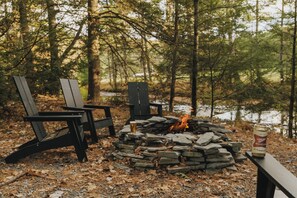 A campfire with logs and two Adirondack chairs.