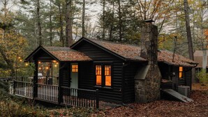 Une cabane rustique avec une cheminée en pierre, un revêtement extérieur en bois et une véranda décorée de guirlandes lumineuses.