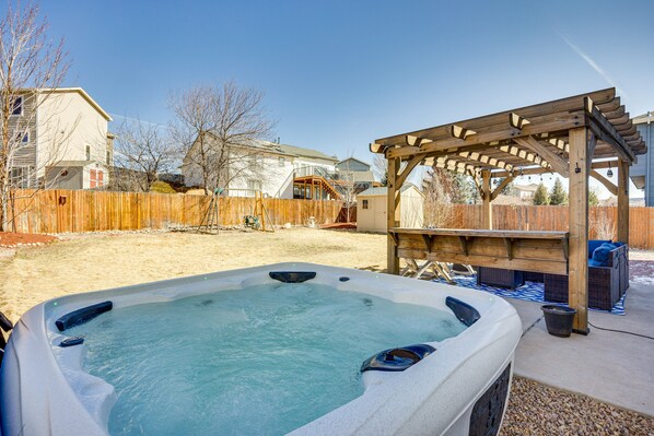 Relax in the backyard hot tub surrounded by a shaded pergola and wooden deck.