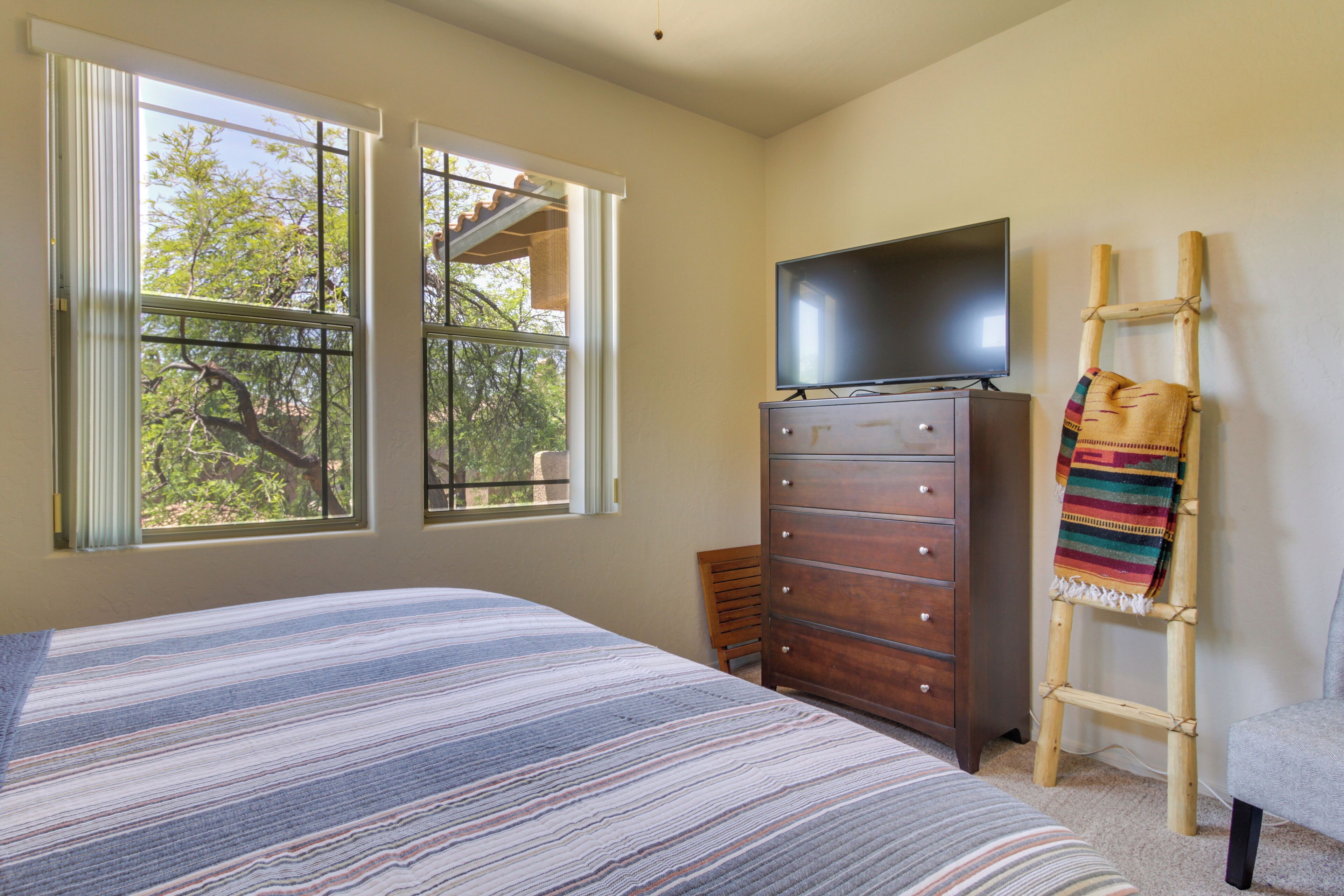 A bedroom with a bed, a dresser, a television, and a window with a view of trees.