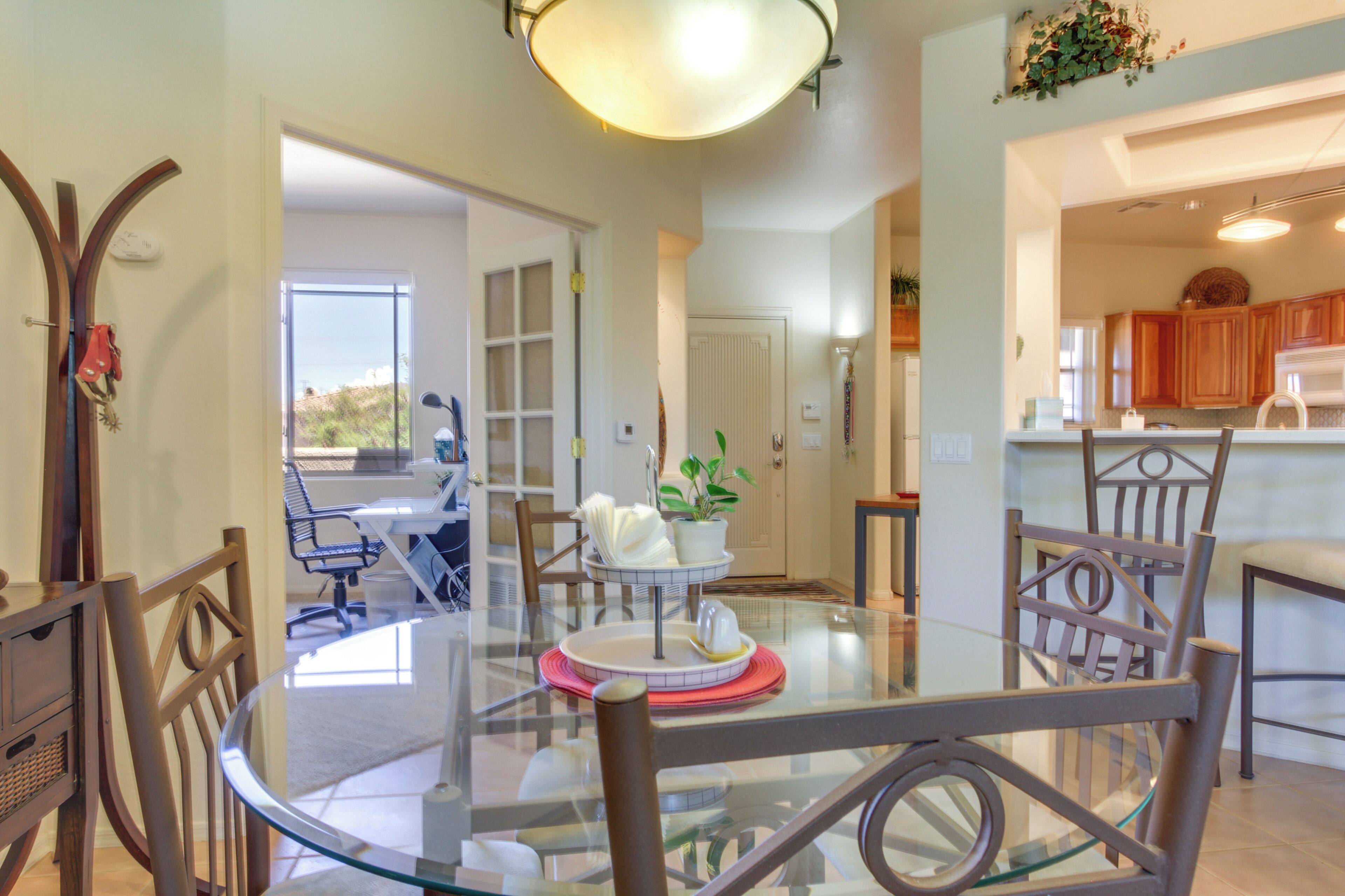 A dining area with a glass table, chairs, and a view of the kitchen.