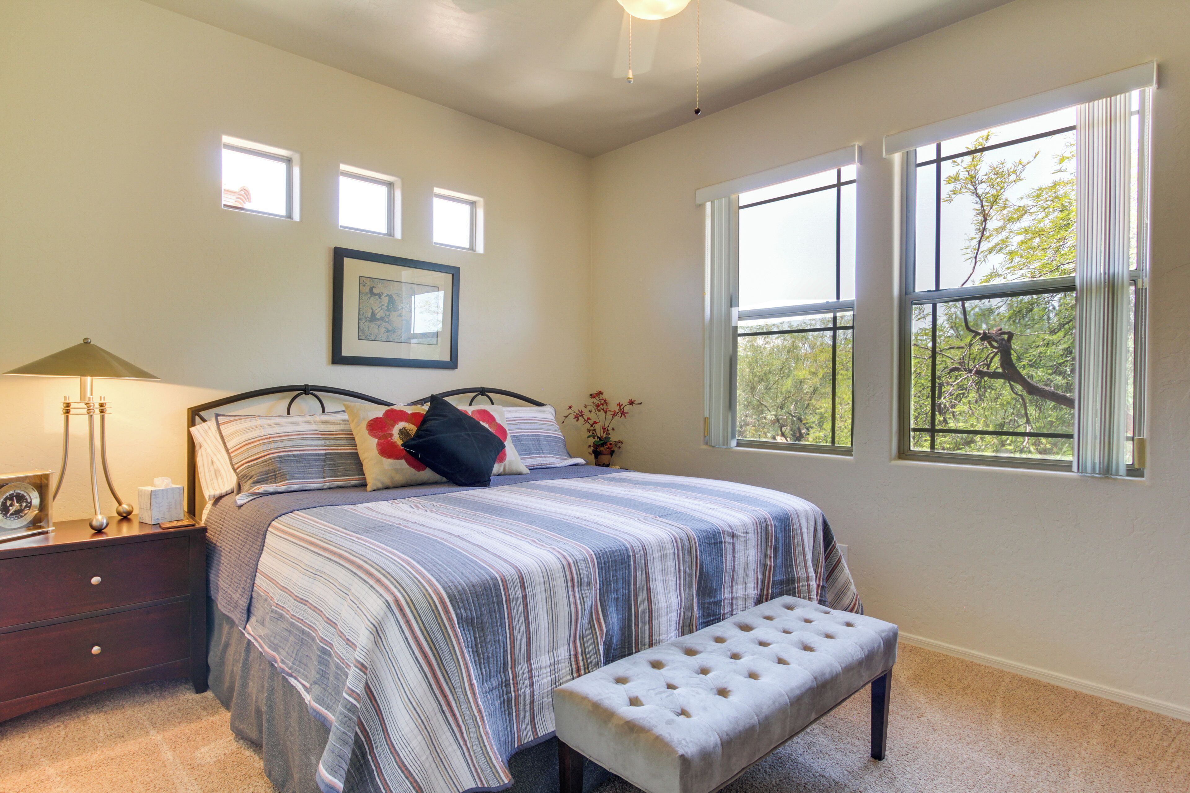 A bedroom with a bed, bedside table, lamp, and windows.