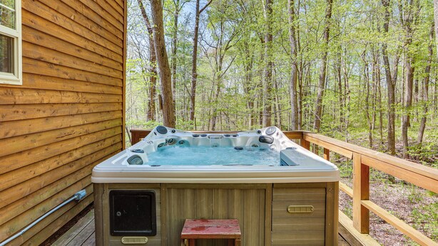 Una cabaña de madera con jacuzzi en una terraza rodeada de árboles.