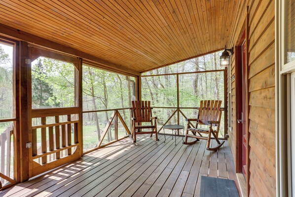 A wooden deck with rocking chairs and a small table, surrounded by a forest. - Dreamy Indiana Cabin Rental w/ Shared Amenities! (Taswell)