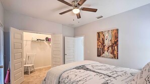 Une chambre à coucher avec un lit, un ventilateur de plafond, une porte blanche, une chaise et un tableau accroché au mur.